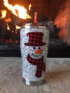 a tumbler with a snowman on it sitting in front of a fire place