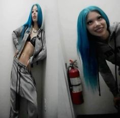 a woman with blue hair standing next to a fire hydrant and posing for the camera