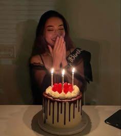 a woman sitting in front of a cake with candles on it and her hands covering her mouth