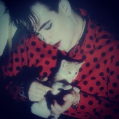 a man in red and black shirt holding a cat with his right hand on the kitten's chest