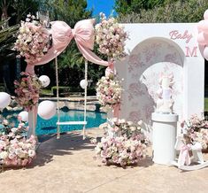 an outdoor wedding setup with pink and white flowers on the arch, balloons in the background