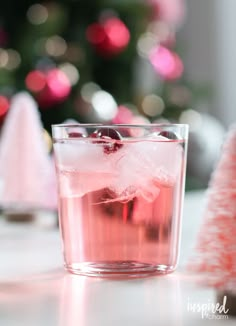 a glass filled with ice and cranberries on top of a table next to a christmas tree