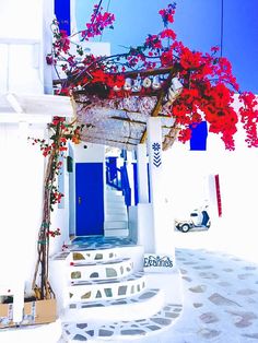 a white building with red flowers growing on it's roof and steps leading up to the door