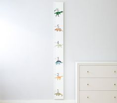 a child's growth chart with dinosaurs on it next to a dresser and bed