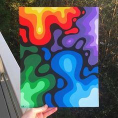 a person holding up a colorful piece of art in front of some trees and bushes