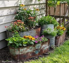 several metal containers filled with flowers on the side of a house's wall and grass