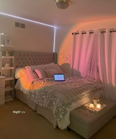 a bed with a laptop on top of it in a room that has pink curtains