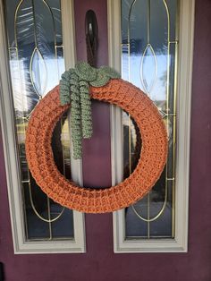 an orange crocheted wreath hangs on the front door of a purple house with glass doors