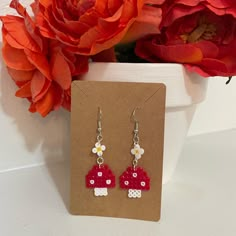 a pair of red and white earrings sitting on top of a card next to flowers