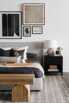 a bed sitting in a bedroom next to a table and pictures on the wall above it