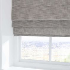 an open window with roman blind in grey linen, overlooking the city skyline and mountains