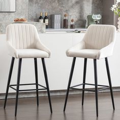 two white bar stools sitting in front of a counter