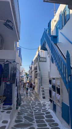 people walking down an alley way with blue shutters on the buildings and stairs leading up to them