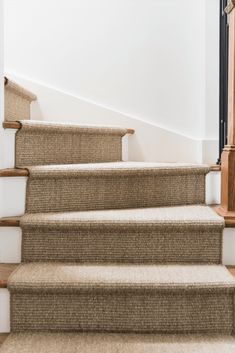 the carpeted stairs are lined with wooden handrails and beige runnering, along with white walls