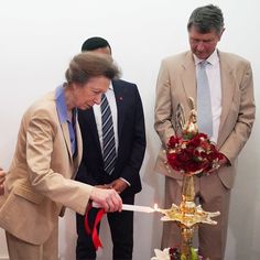 two men in suits and one woman cutting a cake with a red ribbon on it