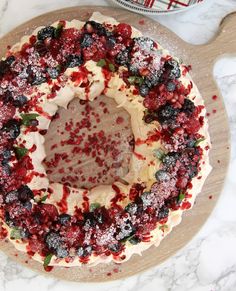 a cake with white frosting and berries on top sitting on a cutting board next to a knife