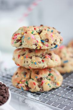 chocolate chip cookies with sprinkles are stacked on a cooling rack next to a bowl of milk