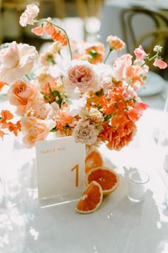 an arrangement of flowers and oranges in a vase on top of a table with a place card