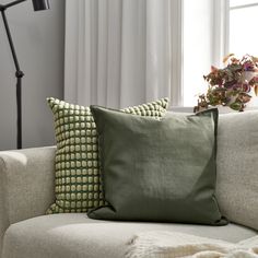 a couch with two pillows on it next to a lamp and potted plant in the corner