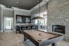 a pool table in the middle of a living room with an open fireplace and dining area