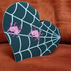 a heart shaped box with two pink crabs in the center on a black web - covered surface