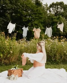 a woman sitting on top of a blanket in front of clothes hanging from a line