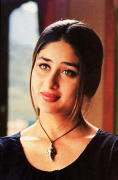 a woman wearing a black top with a necklace on her neck and looking at the camera