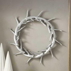 a wreath made out of branches on the wall next to a white vase with flowers in it