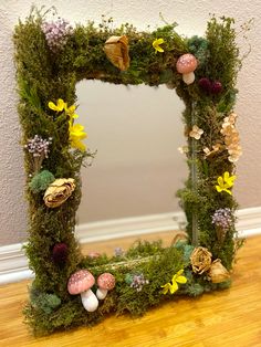 a moss covered frame with mushrooms, flowers and other things in it on the floor