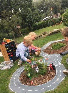 two young boys playing with toy cars in the grass on a miniature road and track