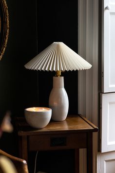 a white lamp sitting on top of a wooden table next to a vase and bowl