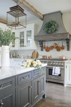 a kitchen with gray cabinets and white counter tops, an oven hood over the stove