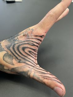 a person's hand with a black and grey tattoo on it, resting on a table