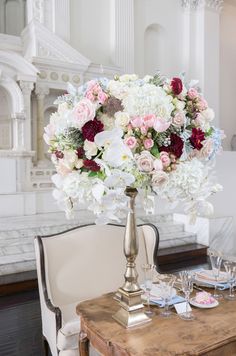 a table topped with a vase filled with flowers next to a white chair and wooden table