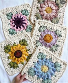 four crocheted coasters with different colored flowers on them and one being held up by a hand