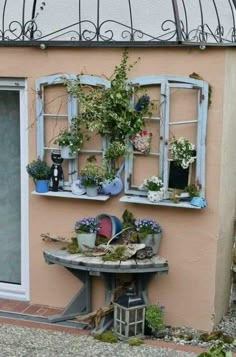 an outdoor table with potted plants on it next to a pink wall and window