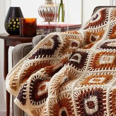 a crocheted blanket sitting on top of a couch next to a vase with flowers