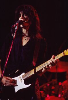 a woman holding a guitar while standing in front of a microphone