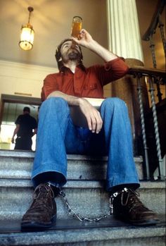 a man sitting on the steps drinking from a beer mug with chains around his ankles