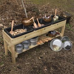 a wooden table with pots and pans on it in the grass next to trees