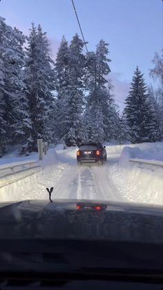 a car driving down a snow covered road in the middle of winter with trees on both sides