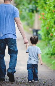 a man holding the hand of a little boy walking down a path