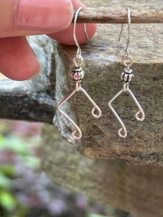 a pair of silver earrings sitting on top of a wooden stick in front of a stone wall