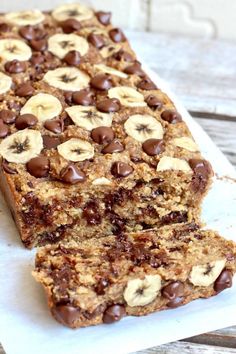 chocolate chip banana bread is cut in half on a piece of parchment paper and sits on a wooden table