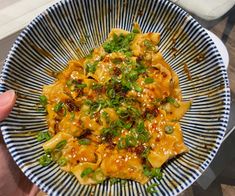 a person holding up a bowl of food with noodles and vegetables in it on a table