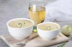 two white bowls filled with soup sitting on top of a cutting board next to an onion