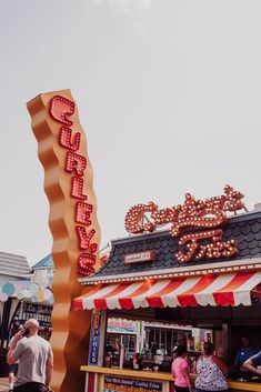 people are walking around in front of a food stand with neon signs on the roof