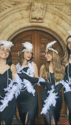 three women dressed in black and white posing for the camera with feathers on their head