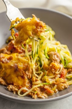 a fork full of spaghetti with meat and vegetables on it, in a gray bowl