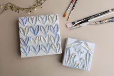 two ceramic tiles sitting on top of a table next to some markers and pencils